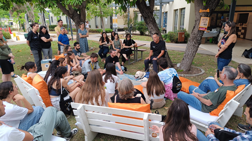 Puppy raisers are seated in a circle under a tree, listening to a lecture at the Center.