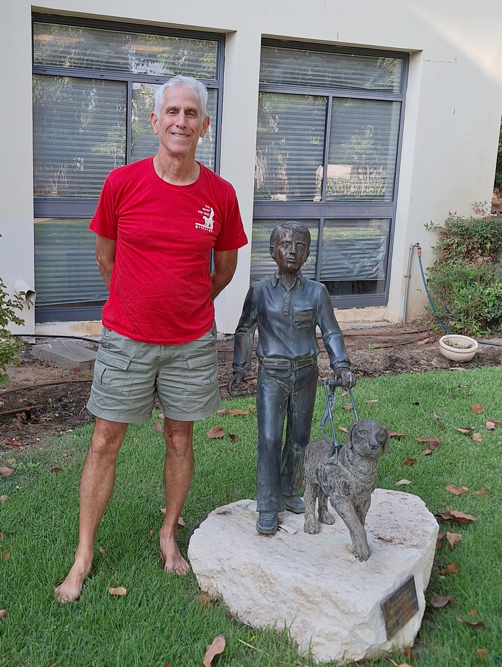 Ephraim is pictured posing next to a statue of a guide dog and young boy located at our Beit Oved campus.